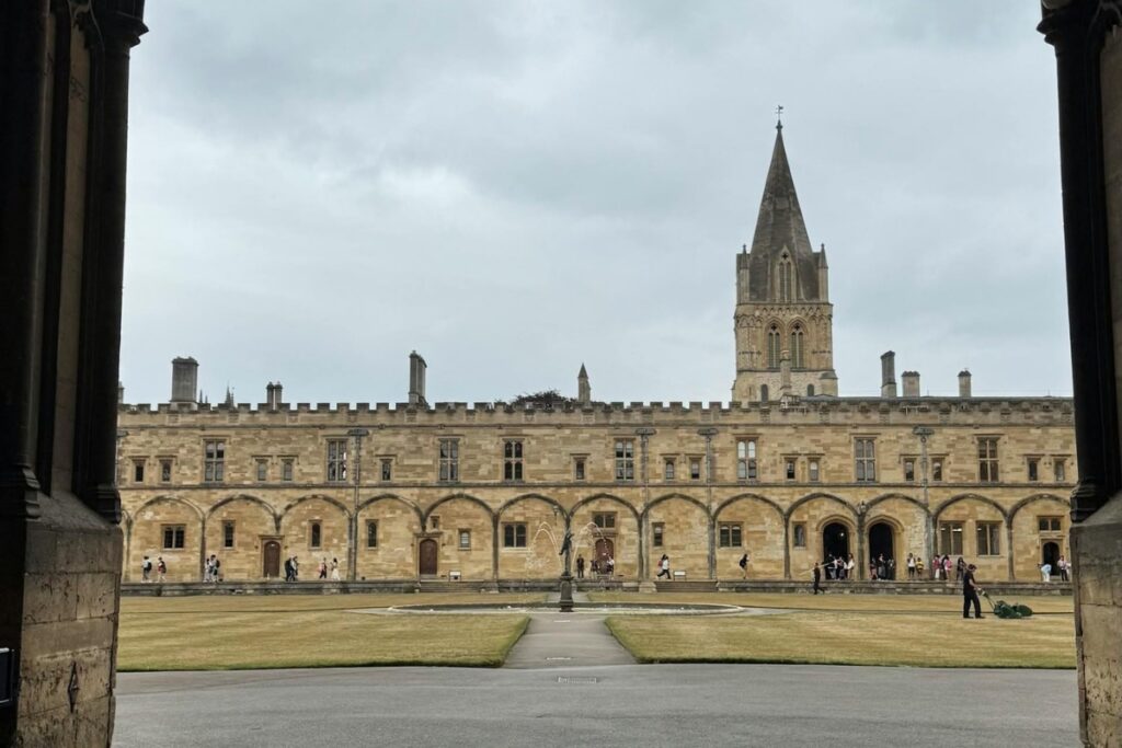 Christ Church com arquitetura gótica e medieval, mostrando arcos de pedra, torre de igreja e jardins centrais sob um céu nublado, que foi cenário real dos filmes de Harry Potter.
